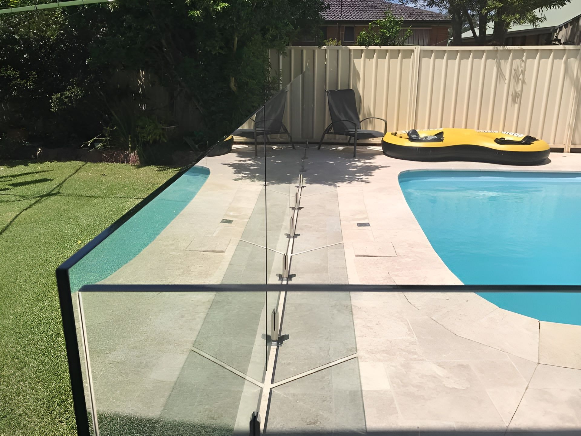 Pool with Glass Fencing and A Yellow Float, Next to A Beige Fence and Greenery — Master Glass & Glazing in Toronto, NSW