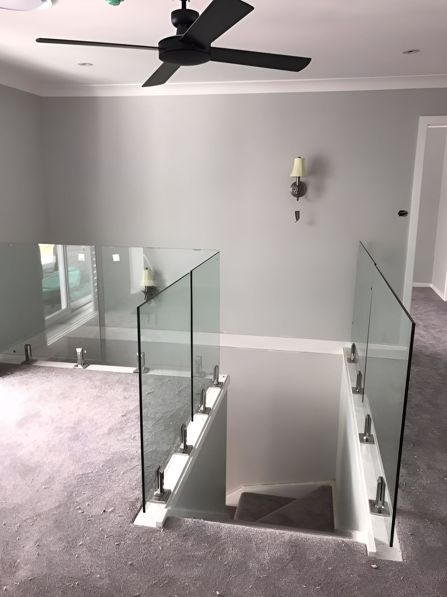 Staircase with Glass Railing, Gray Carpet, White Walls, and A Black Ceiling Fan — Master Glass & Glazing in Mayfield, NSW
