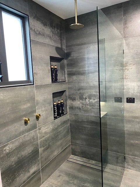 Grey Tiled Shower with Glass Door and Built-In Shelving Holding Toiletries — Master Glass & Glazing in Newcastle, NSW