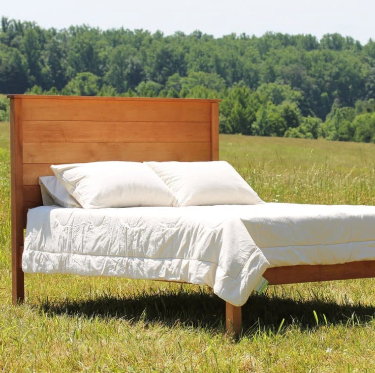 Beautiful natural wood bed frame and 100% natural Mattress are sitting outside under a tree with a beautiful landscape.