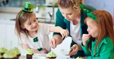 Three children in green St. Patrick’s Day outfits decorating cupcakes at a table