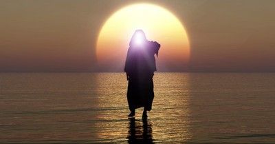 Silhouette of a person standing in shallow water at sunset, with the sun glowing behind them.