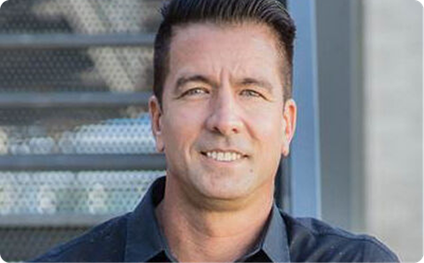 Man smiling in a dark shirt in front of a metal grid background