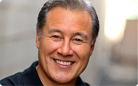 Smiling man in a dark shirt, with gray hair, against a softly blurred background
