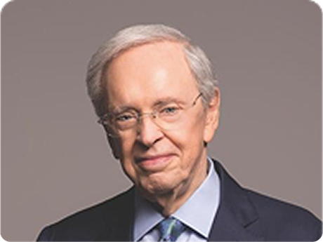 Studio portrait of a man in glasses and a dark suit, smiling against a gray background
