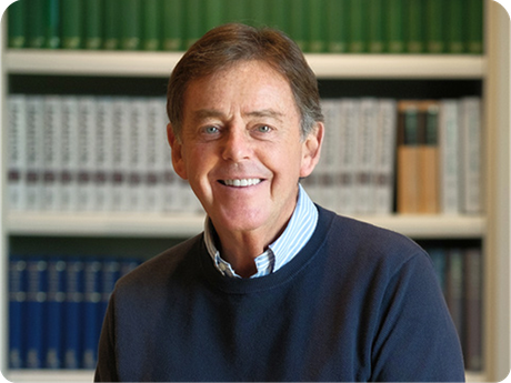 Smiling man in a navy sweater standing in front of bookshelves