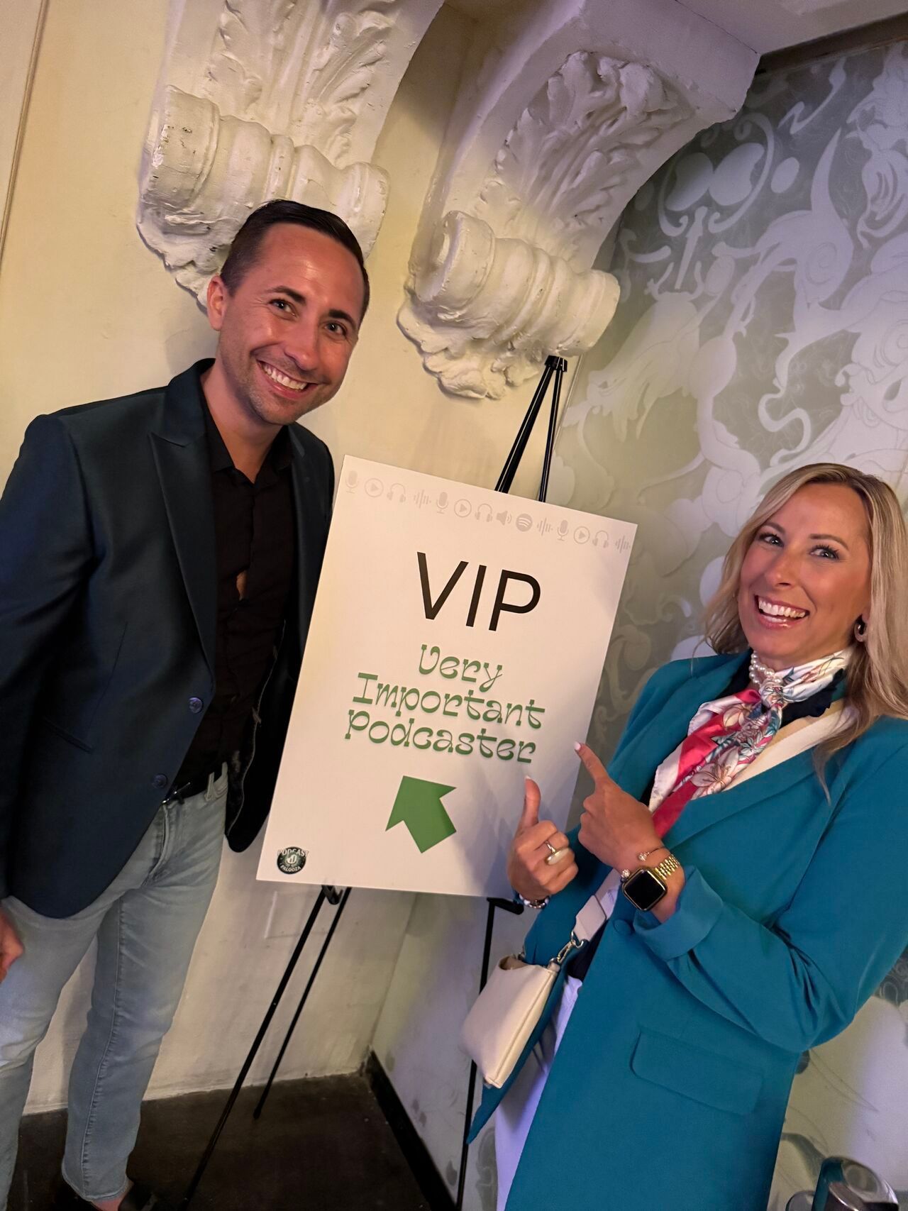 Ronald Harrington and Kristi Fickert pose beside a VIP sign in a decorated indoor venue, smiling and pointing at the board.
