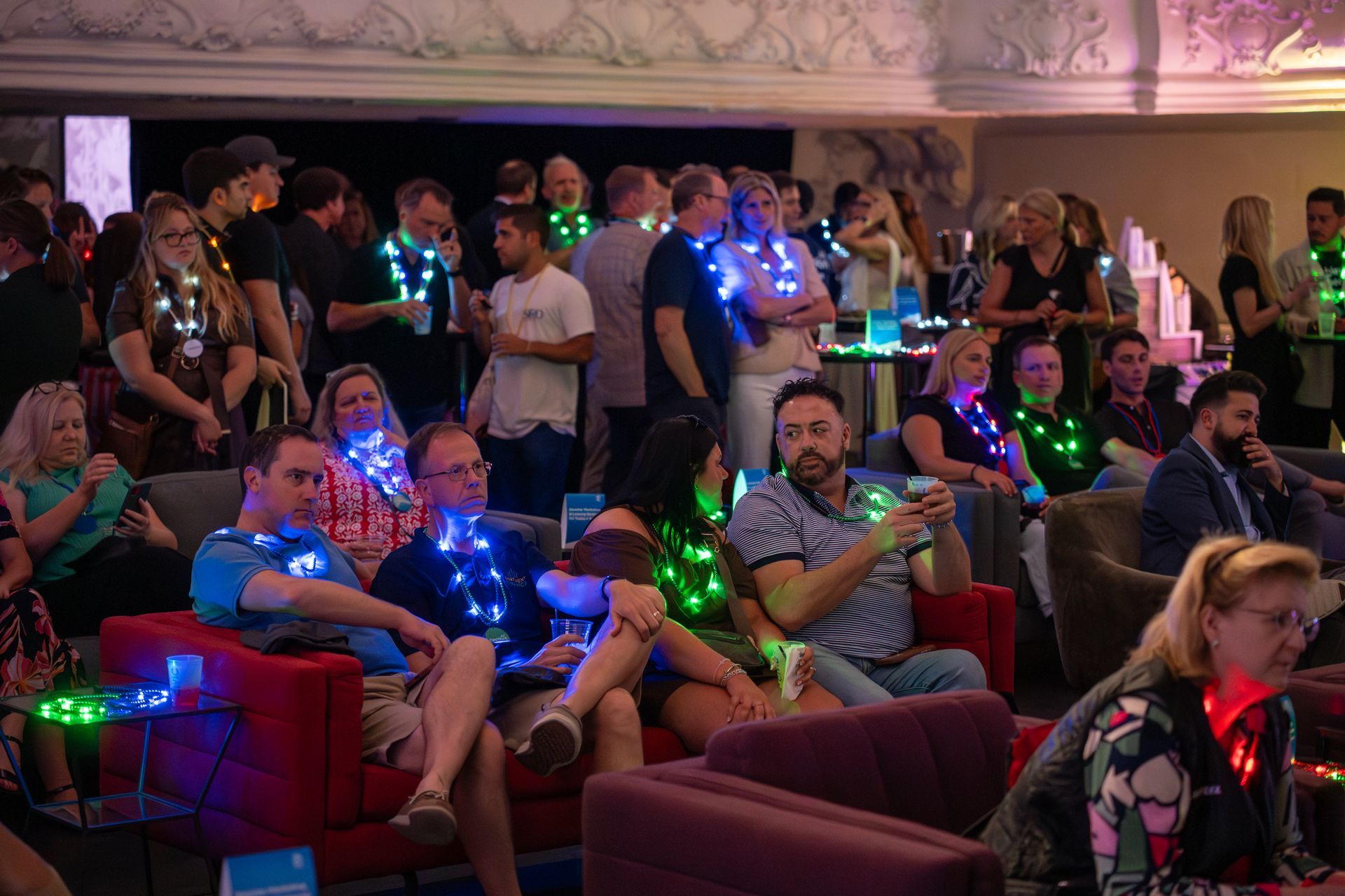 People seated in a dim theater wearing glowing LED necklaces and bracelets during an event