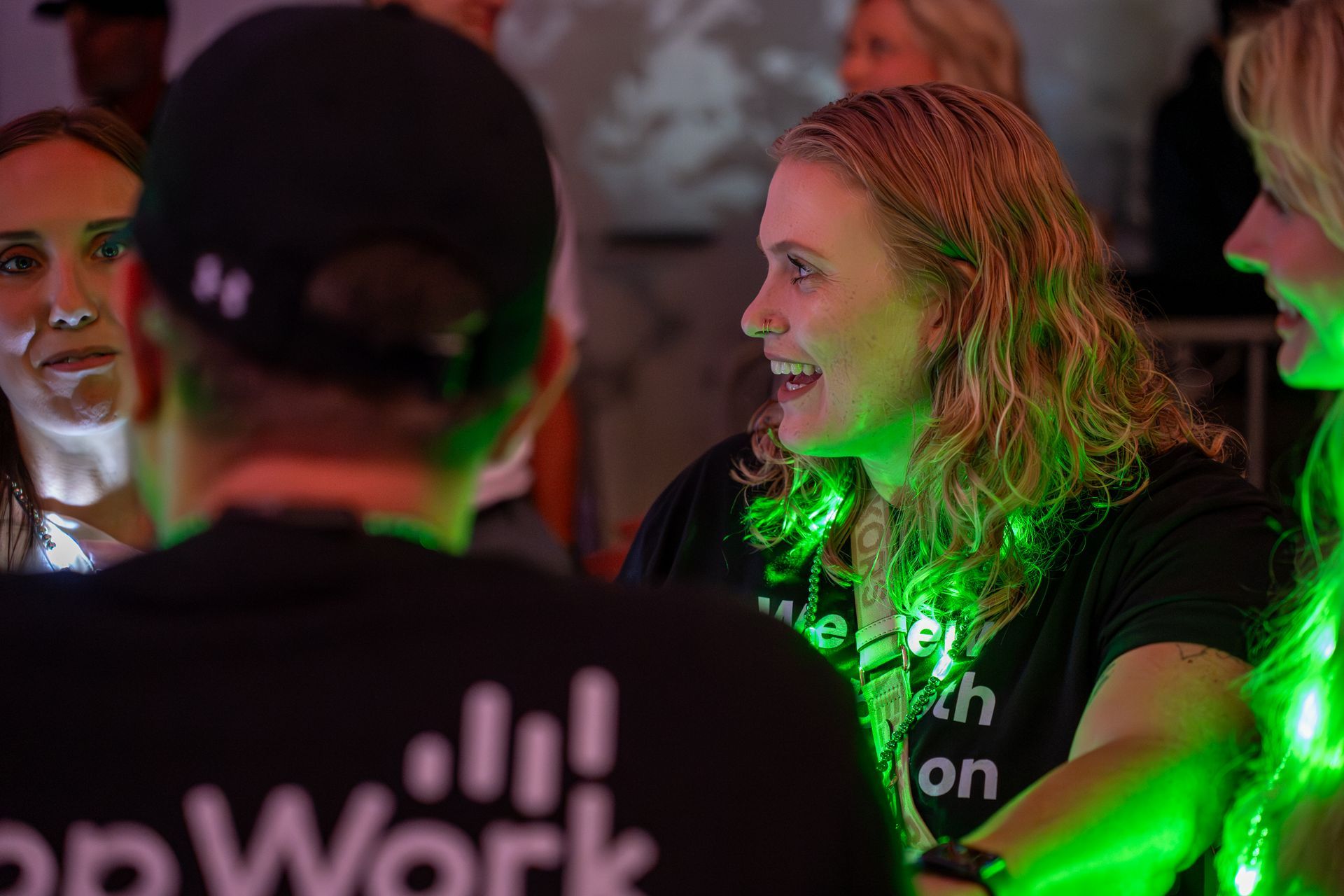 People chatting at a dim event, with green lighting and a “popWork” shirt visible in the foreground