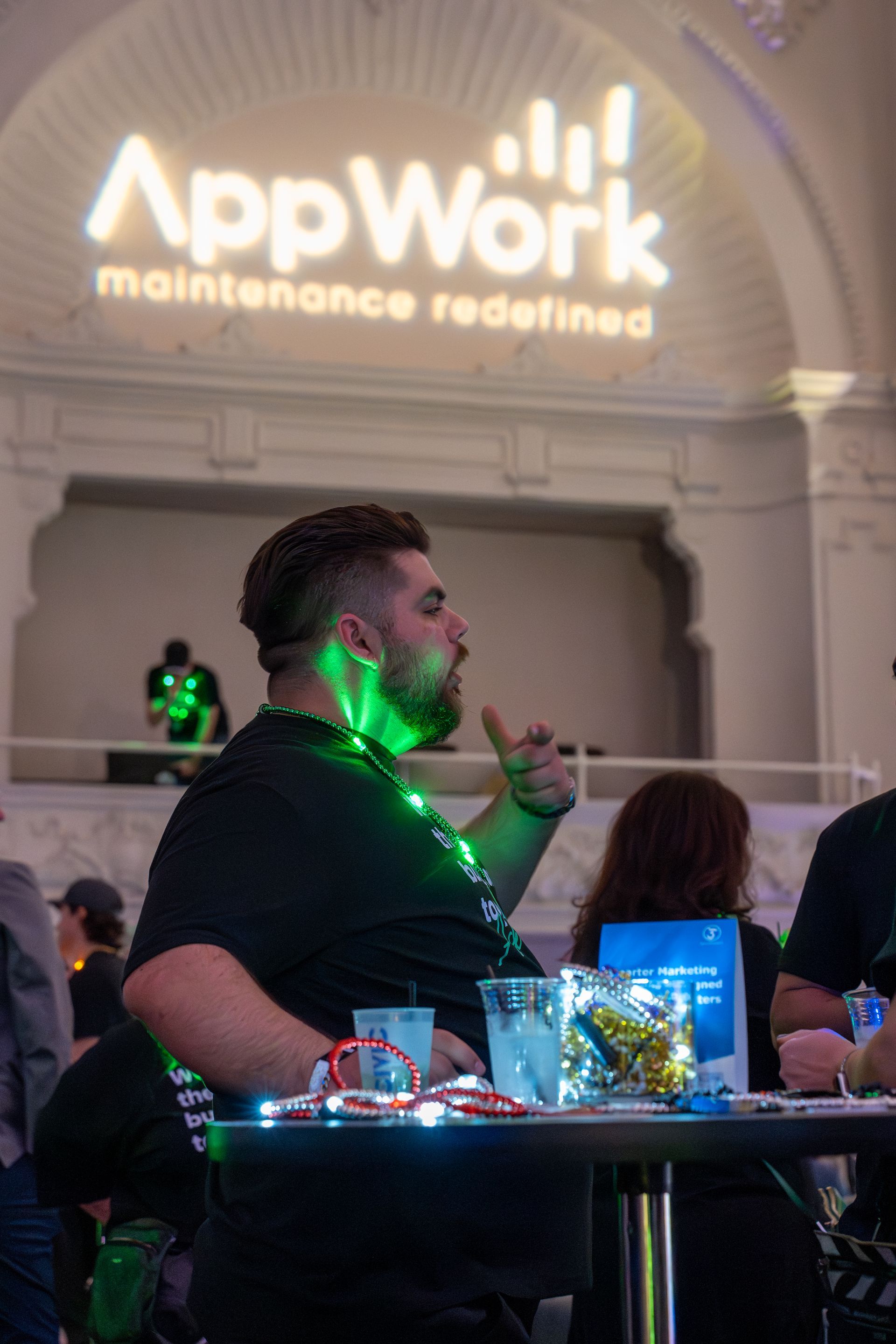 AppWork event attendee at a table with glowing green lights, beneath a “maintenance redefined” projection