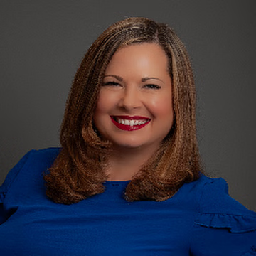Woman with shoulder-length brown hair smiling, wearing a blue top, and red lipstick, against a grey background.