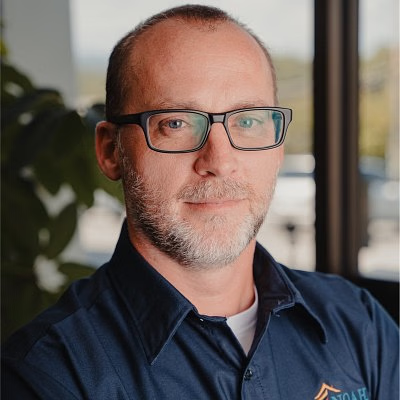 Man with glasses, short hair, and beard, wearing a blue shirt.