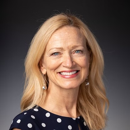 Blonde woman with fair skin smiles at the camera, wearing a navy polka dot top.