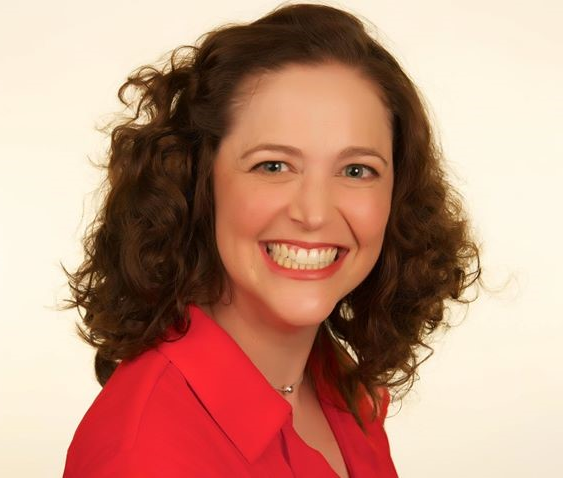 Woman with curly brown hair, wearing a red shirt, smiling widely.