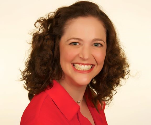 Woman with curly brown hair, smiling widely, wearing a red shirt.