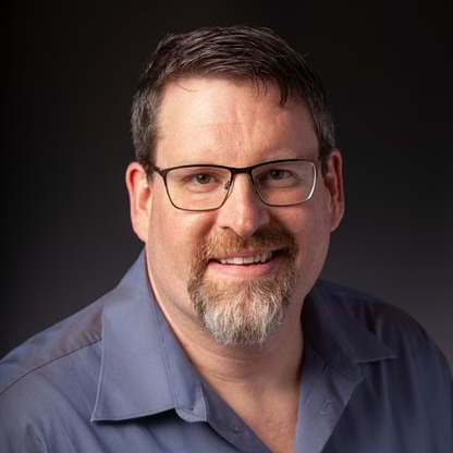 Man with glasses and goatee smiling, wearing a blue shirt.