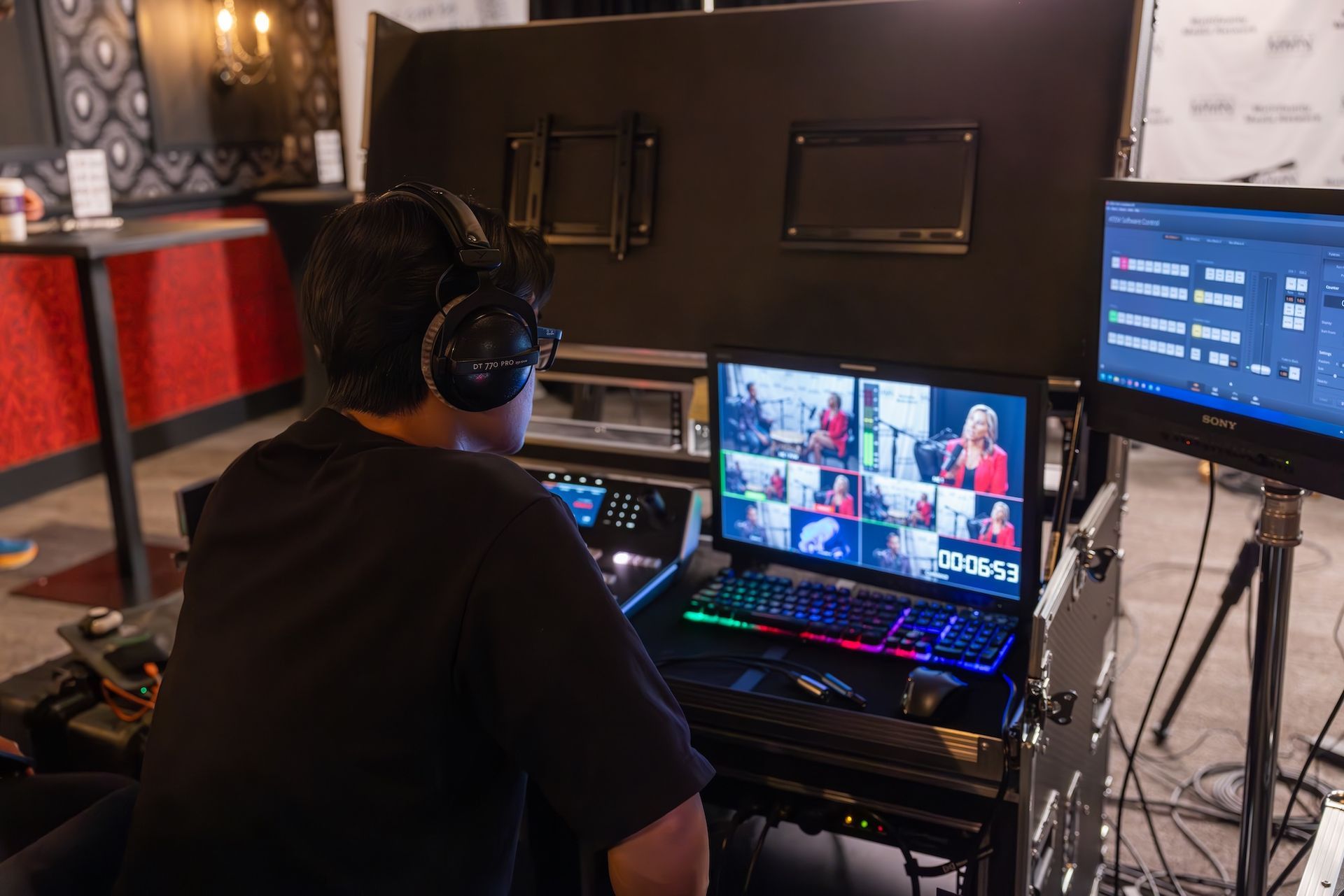 Person wearing headphones operates video equipment, watching a screen with multiple live video feeds.