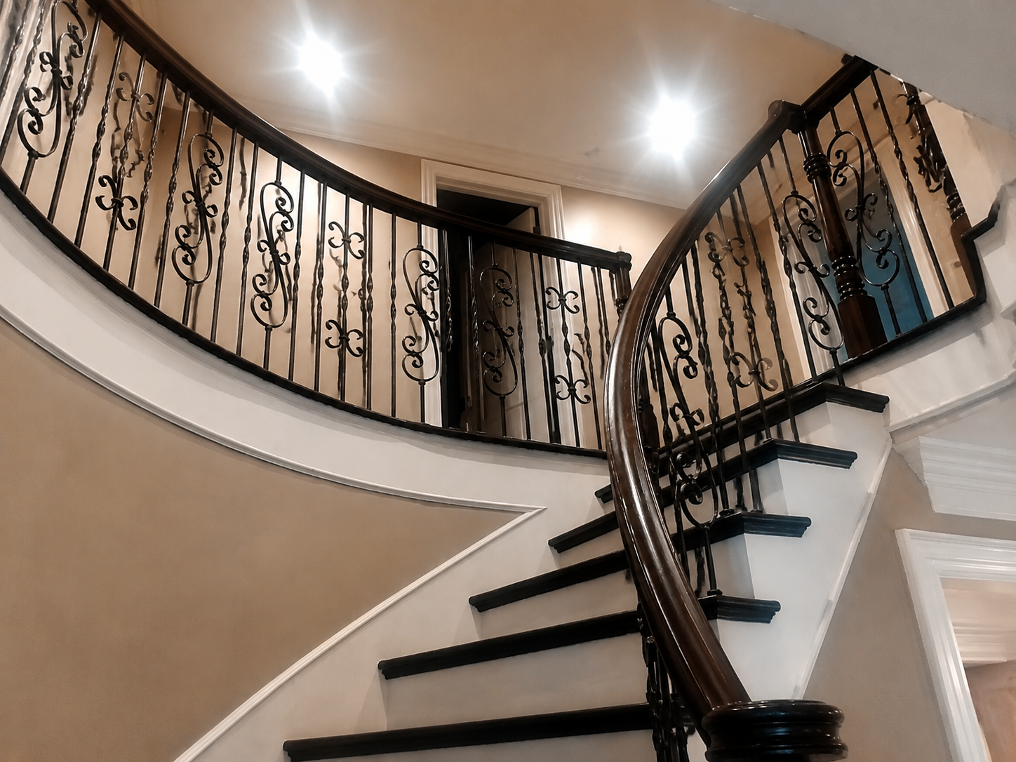 Curved staircase with dark steps and ornate black railing in a beige interior foyer