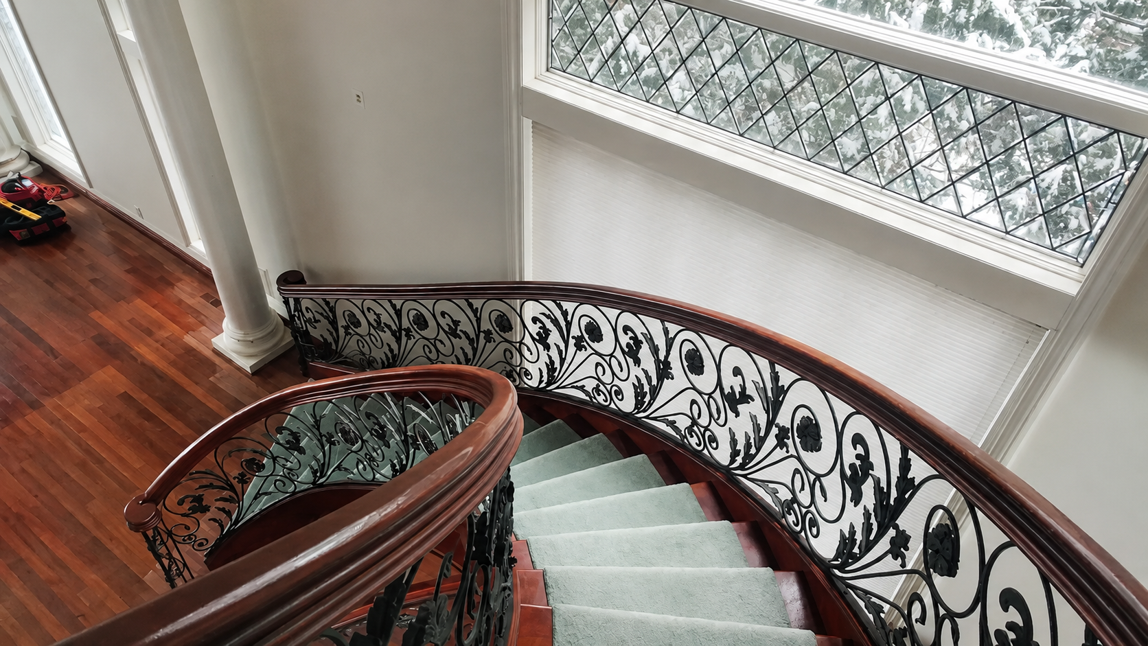 Curved staircase with pale steps, ornate black railing, and large windows overlooking a garden