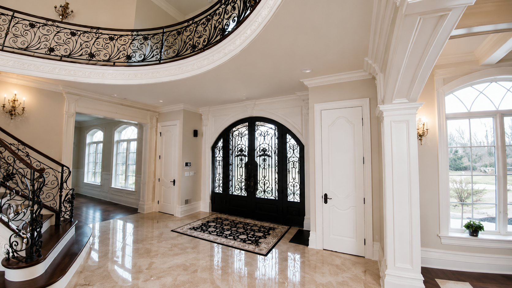 Grand foyer with marble floor, ornate staircase, black double doors, and large windows