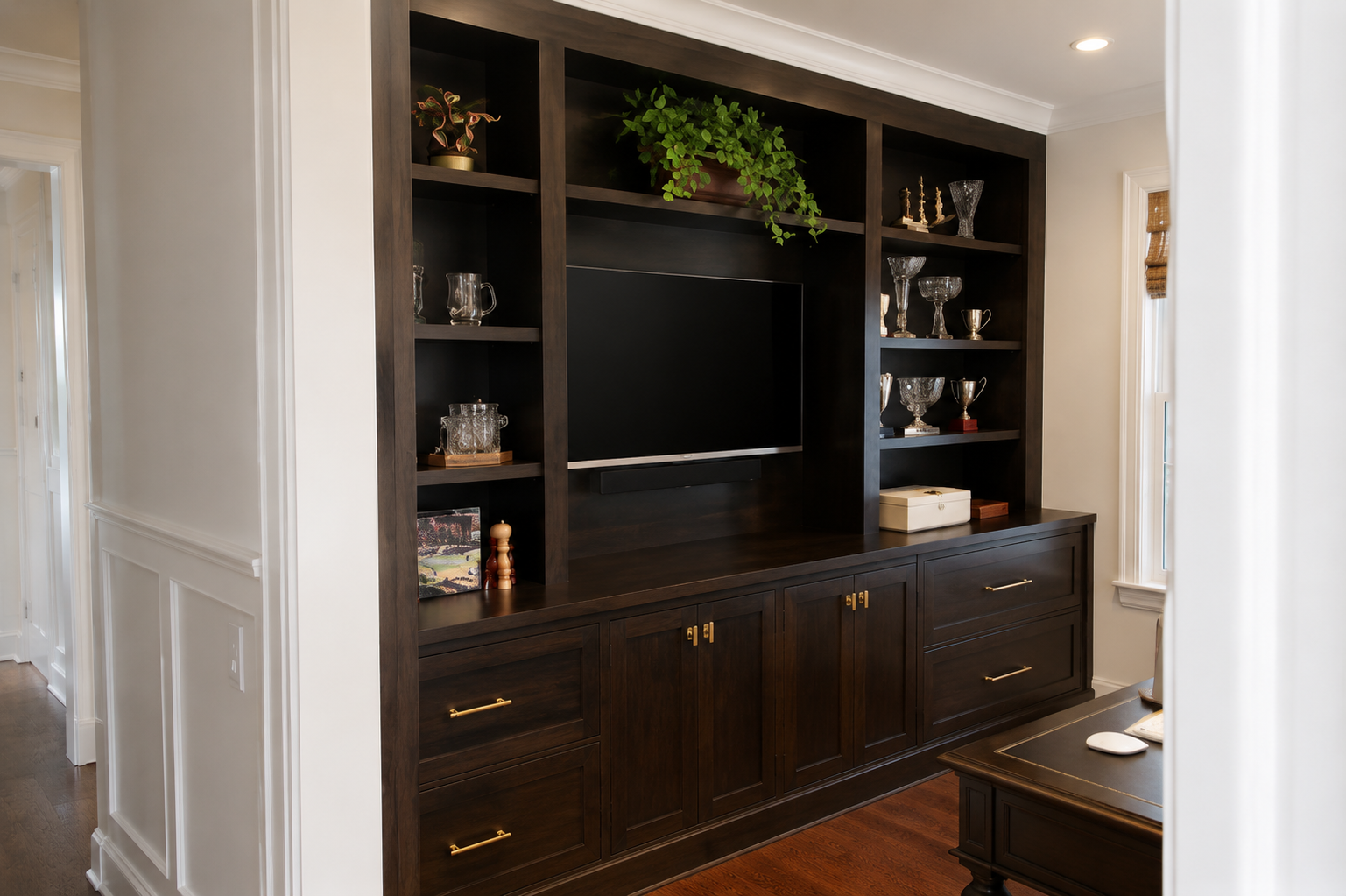 Built-in dark wood entertainment center with TV, shelves, cabinets, and a potted plant in a hallway alcove