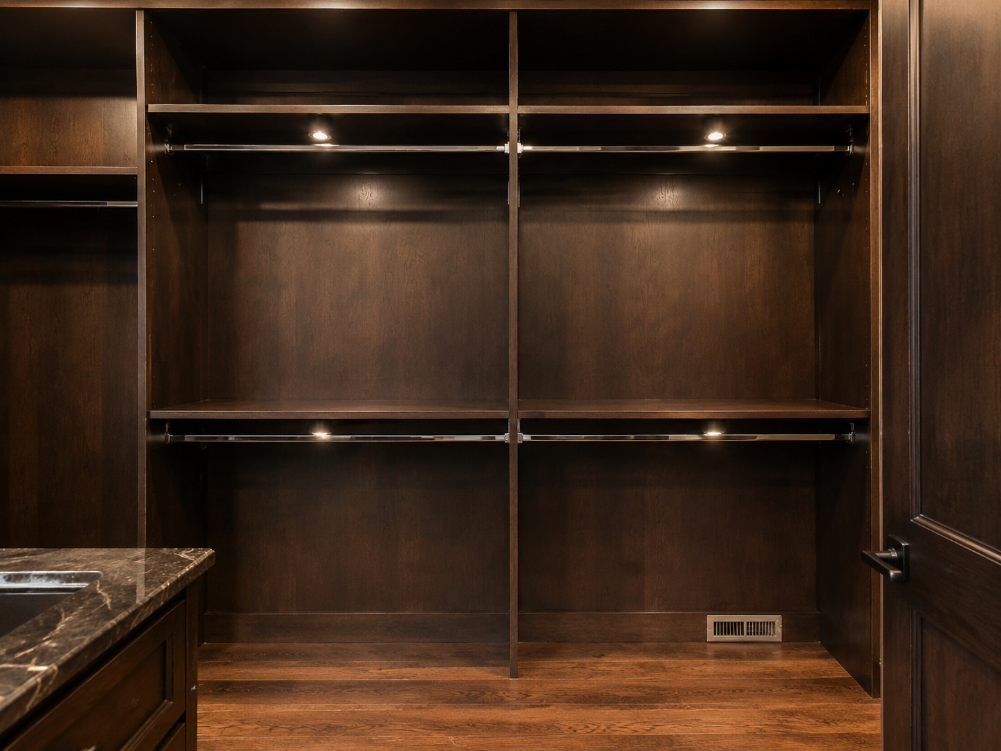 Empty dark-wood walk-in closet with shelves, hanging rods, and a granite countertop on the left.