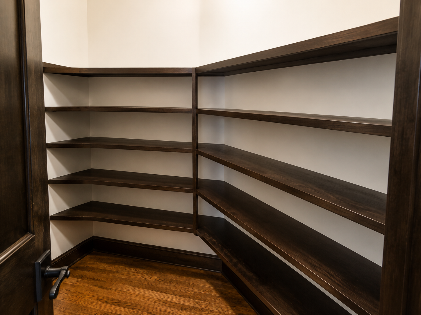 Empty corner shelving unit with dark wooden shelves and a wooden floor, seen in a room.