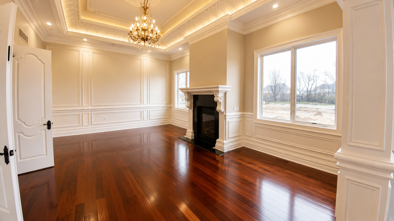 Elegant empty living room with polished hardwood floors, chandelier, fireplace, and large windows