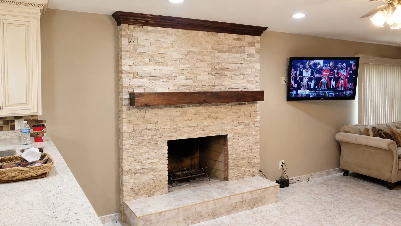 Living room with stone fireplace, mantel, wall-mounted TV, and beige armchair