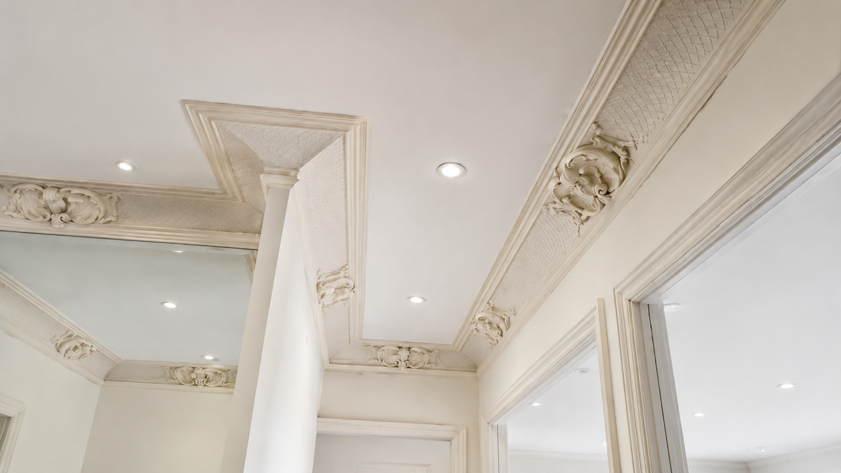 Elegant white interior ceiling with ornate trim, recessed lights, and a sheer curtain near a mirrored wall