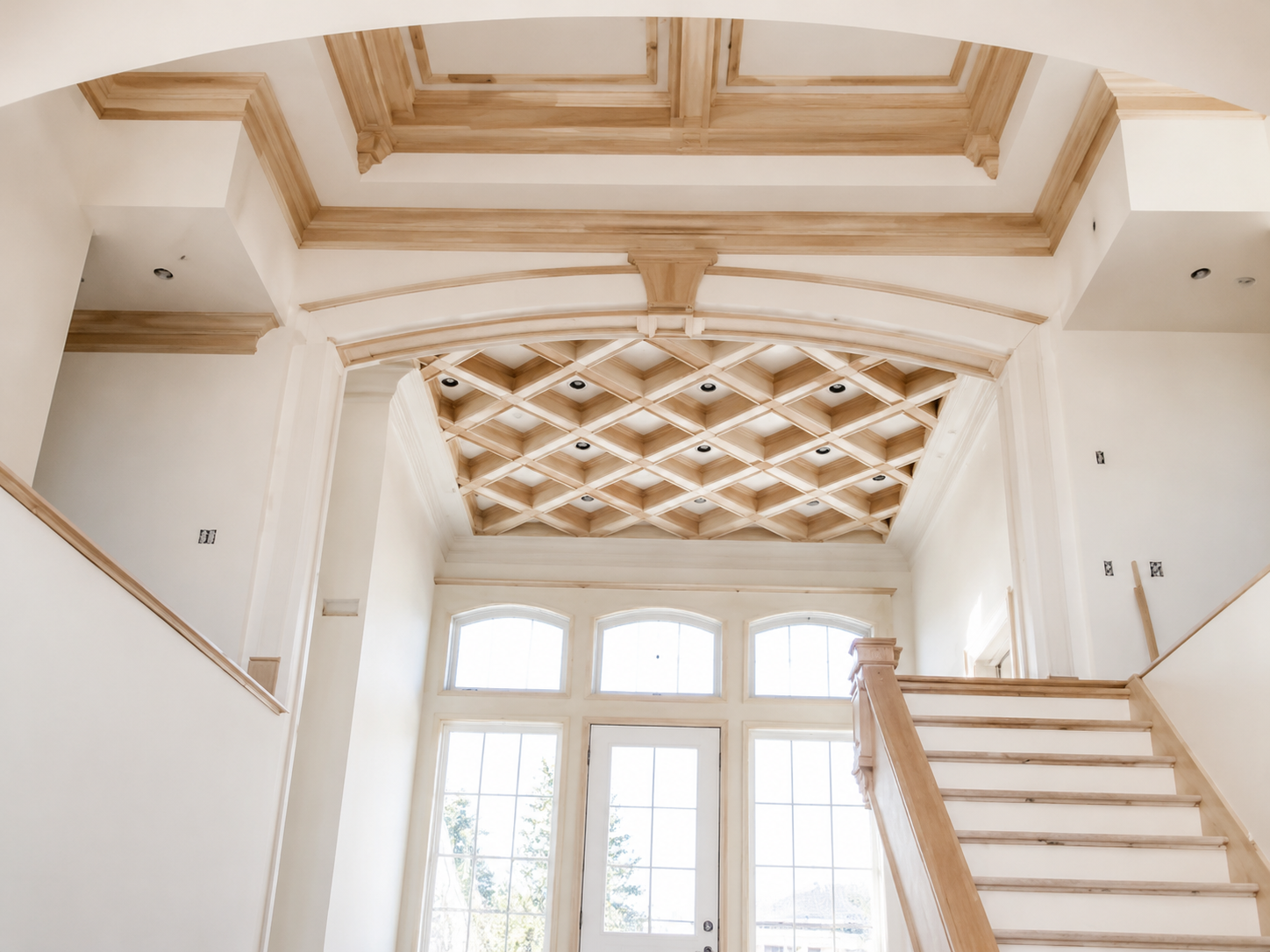 Grand foyer with ornate coffered ceiling, white staircase, and tall arched windows