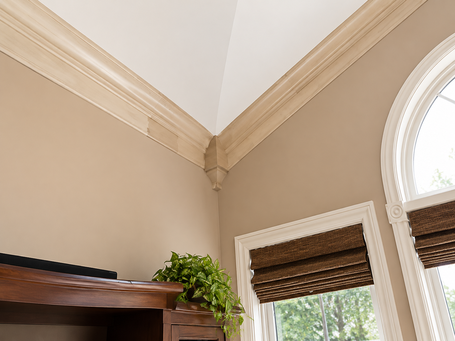 Corner of a beige room with crown molding, arched window, and wood blinds above a fireplace mantle with greenery