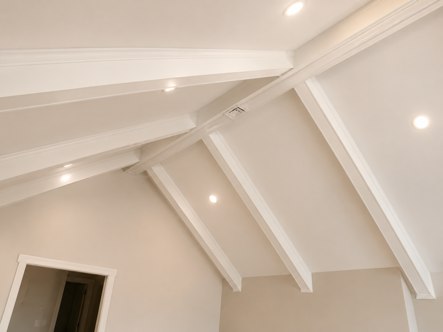 White vaulted ceiling with exposed beams and recessed lights above a doorway