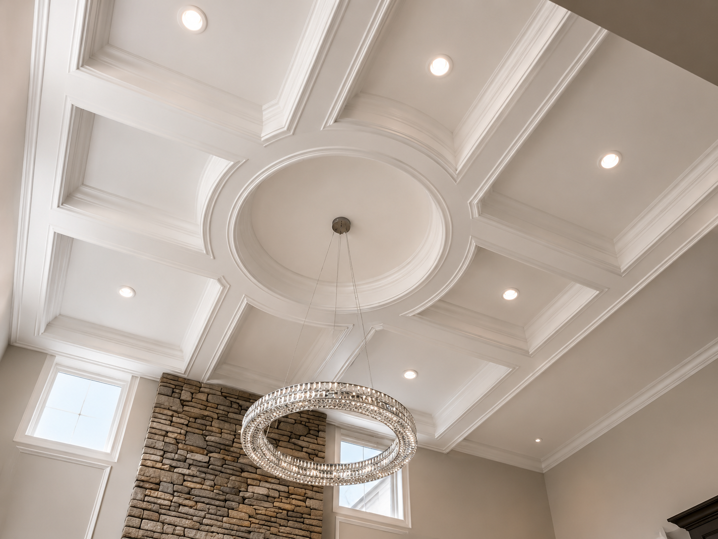 Coffered white ceiling with recessed lights and a modern chandelier above a mosaic-tiled wall