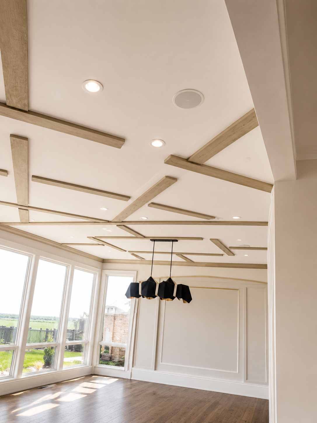 Bright modern empty living room with white ceiling beams, recessed lights, large windows, and hanging pendant lamps