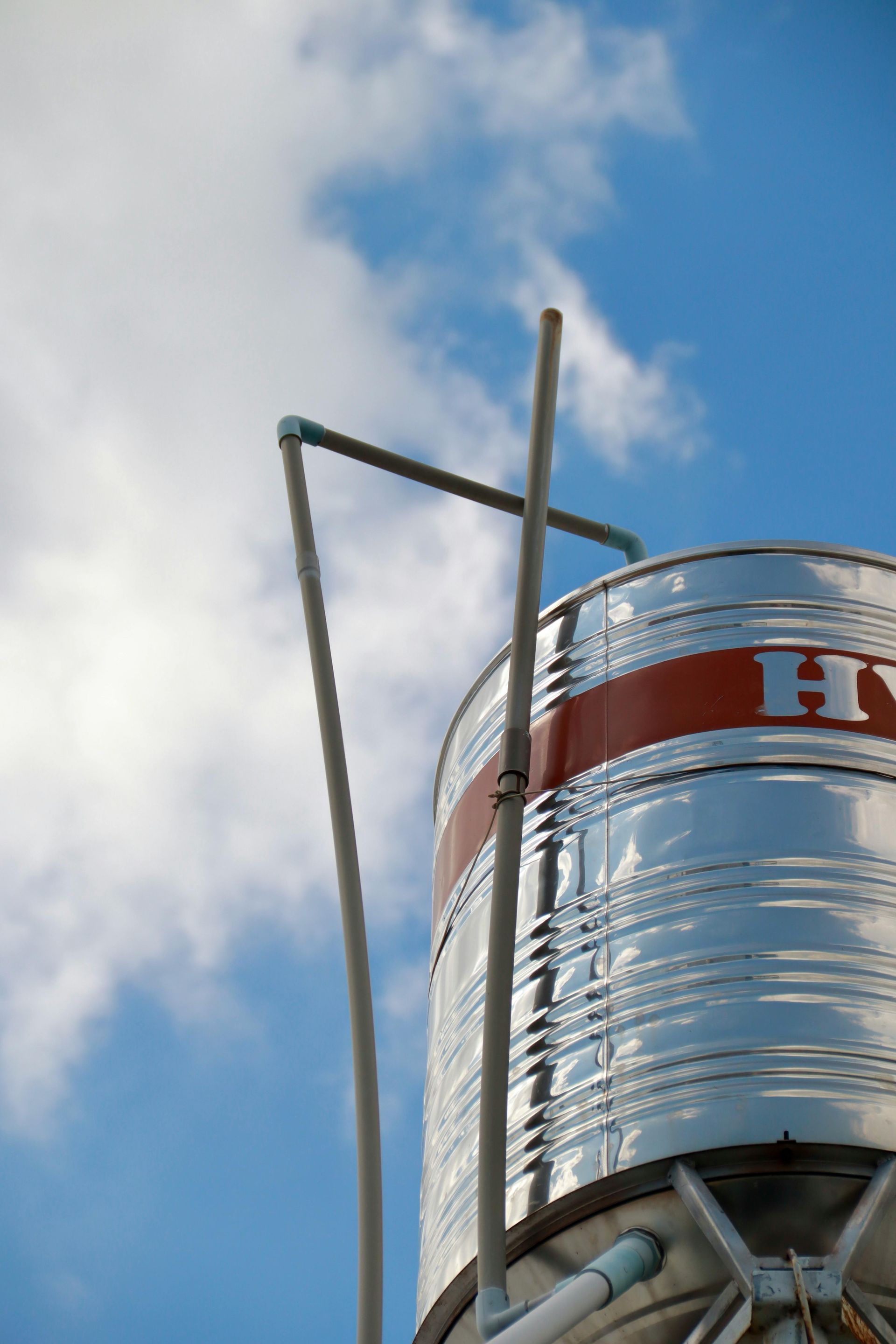 Tall silver water tank against a blue sky with clouds and a red stripe near the top