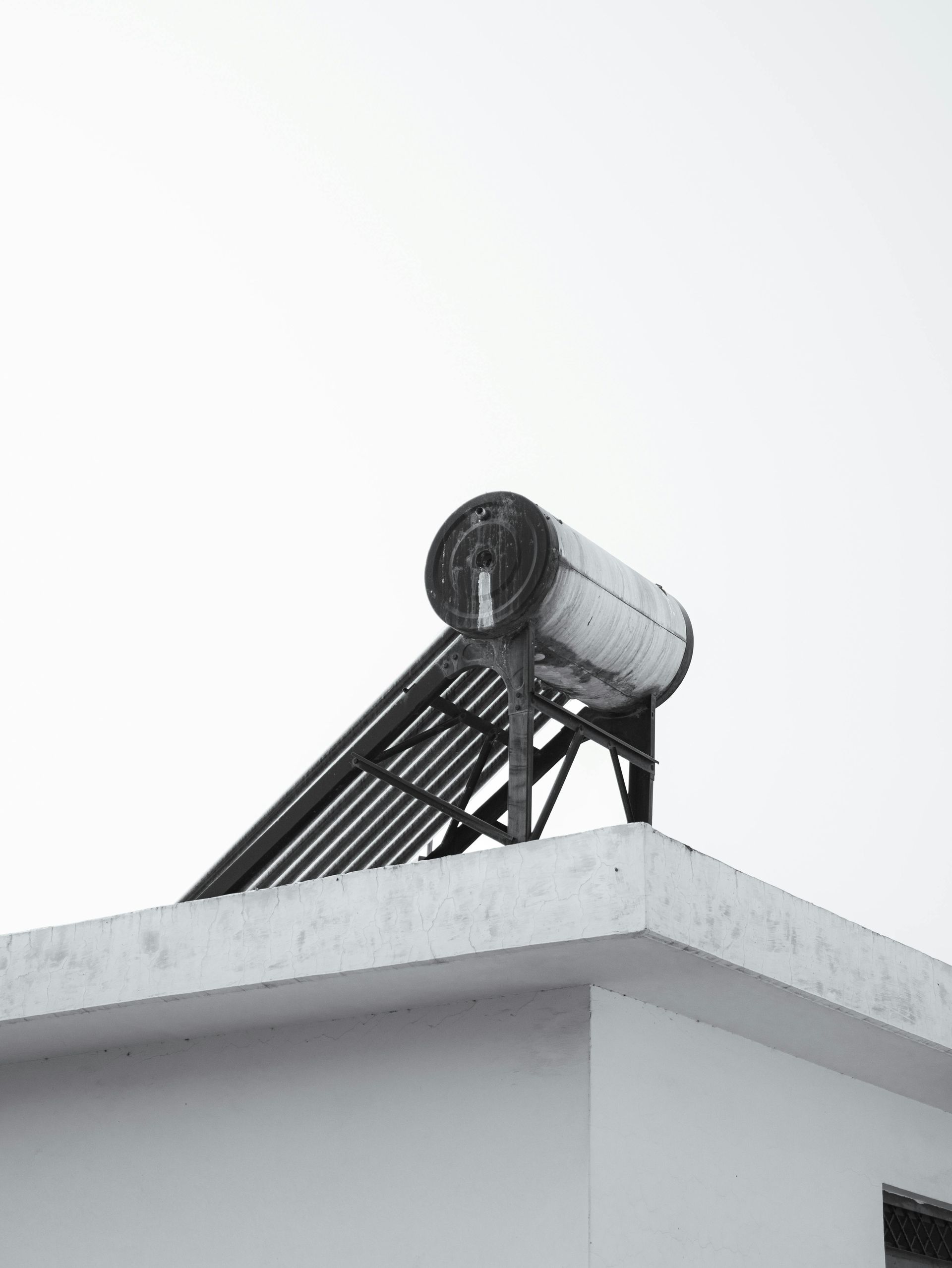 Solar water heater mounted on a white rooftop against a bright sky.