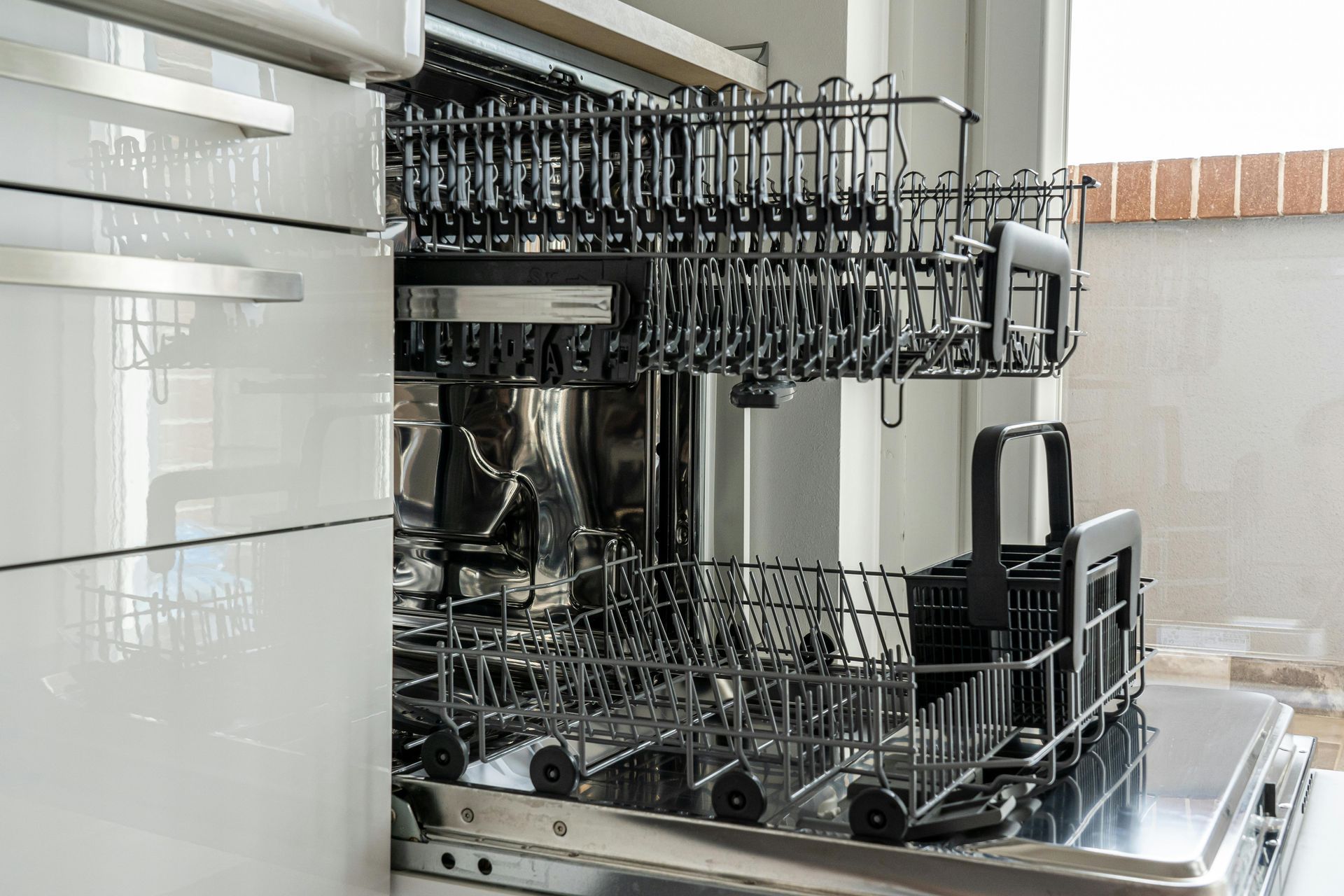 Open dishwasher rack loaded with black utensils and dishes in a modern kitchen