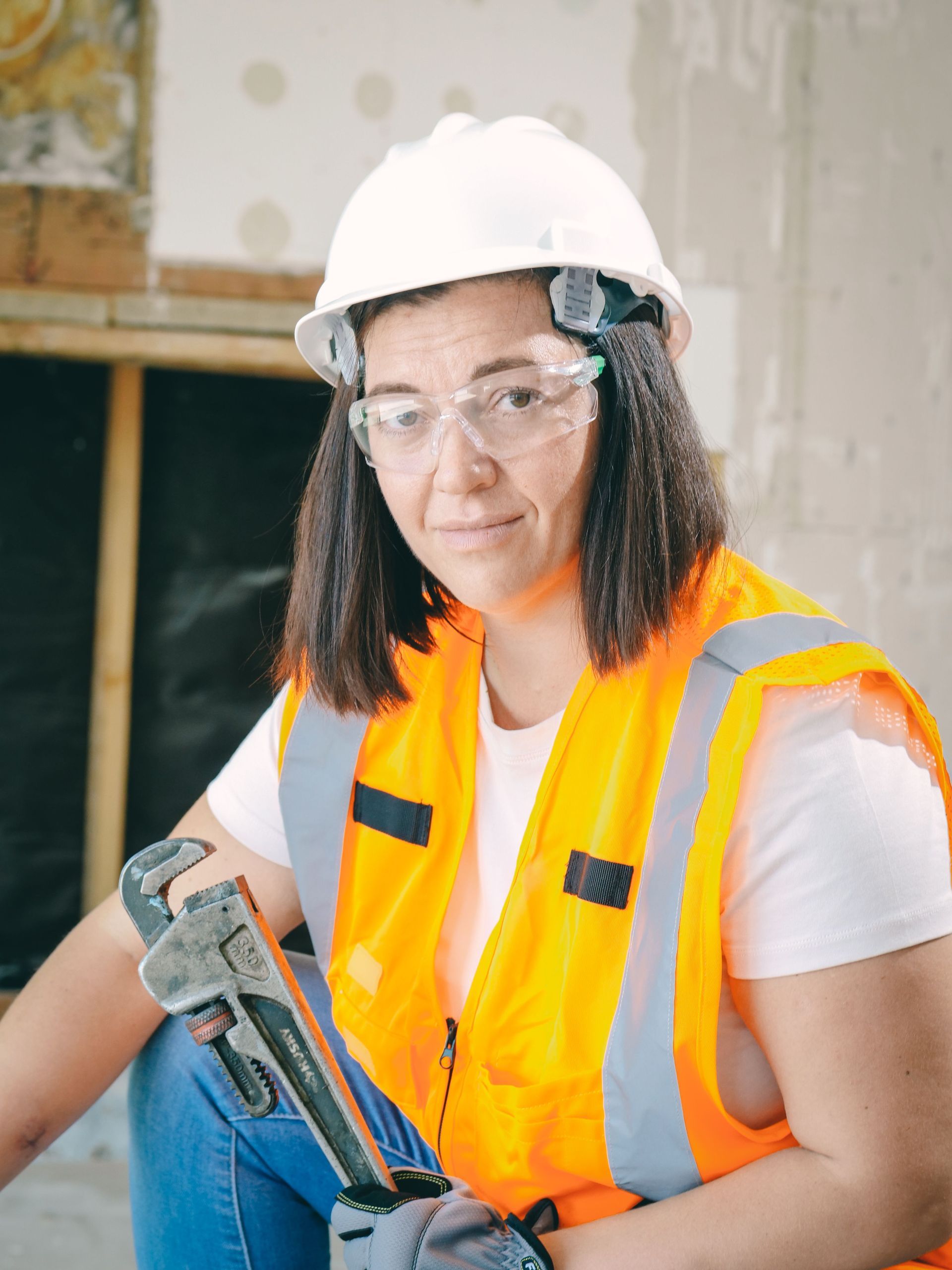 Obrero de la construcción con casco y chaleco de seguridad sosteniendo un taladro eléctrico en el interior.