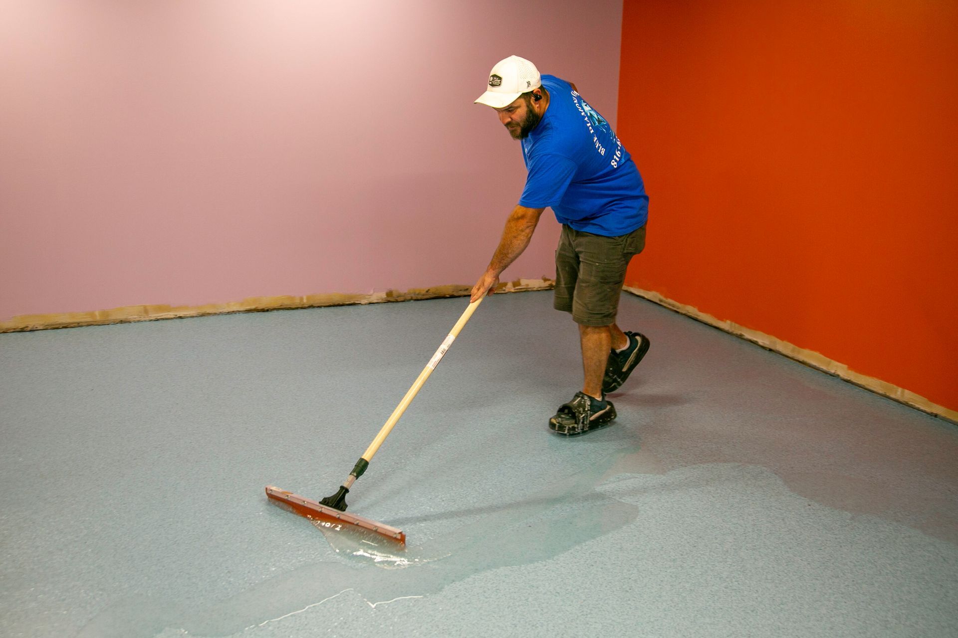 Person squeegeeing water from a car wash bay floor near a car.
