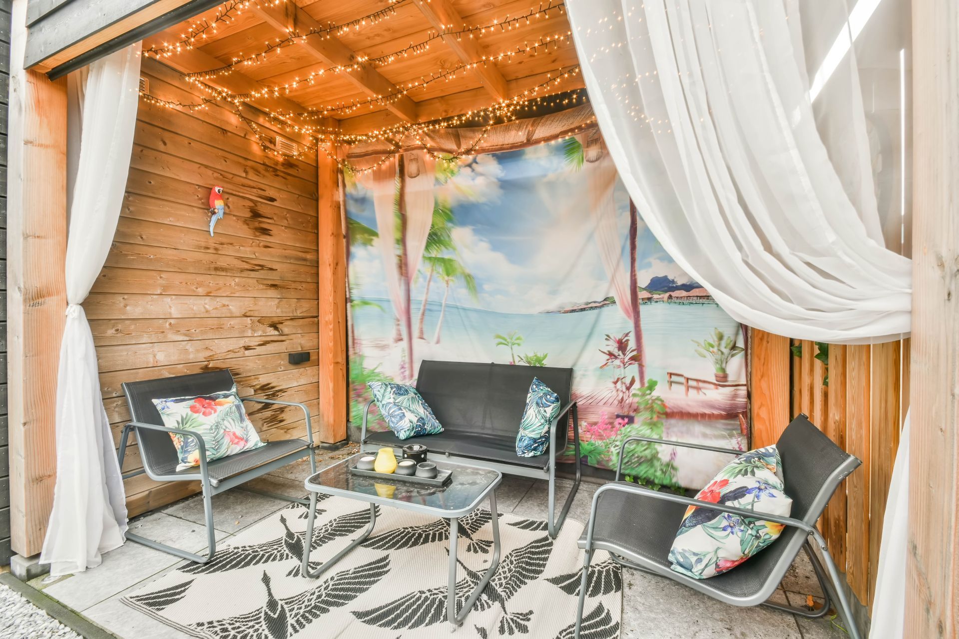 Outdoor seating area with gray furniture, a beach-themed backdrop, draped curtains, and string lights.