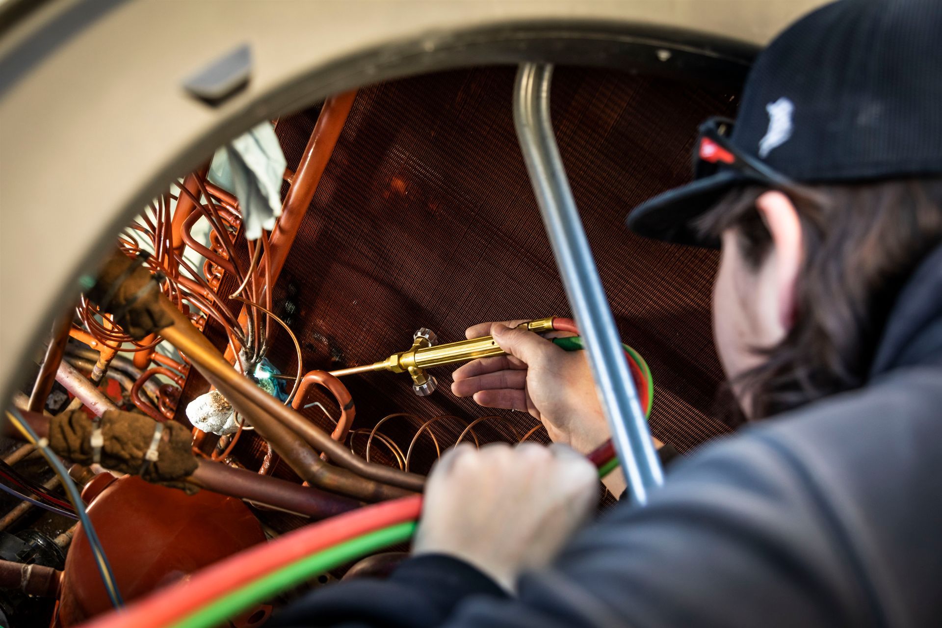 A Thompson Heating and Cooling technician is working on a machine with a welding torch.
