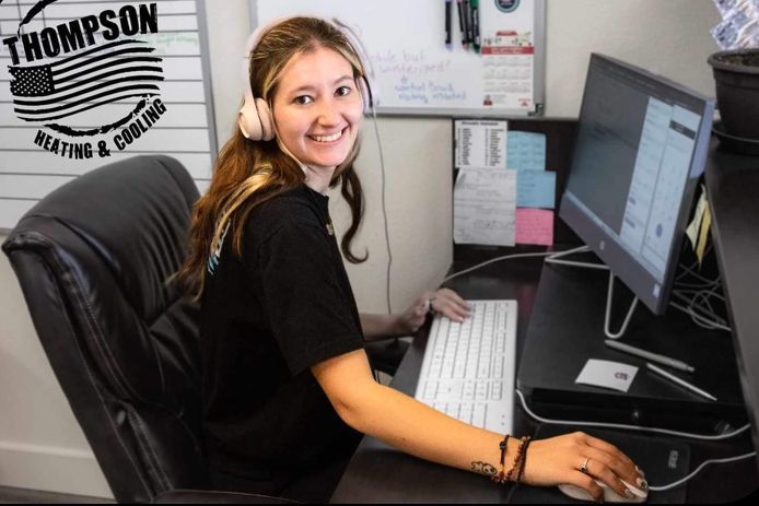 A Thompson Heating and Cooling employee wearing headphones is sitting at a desk in front of a computer.