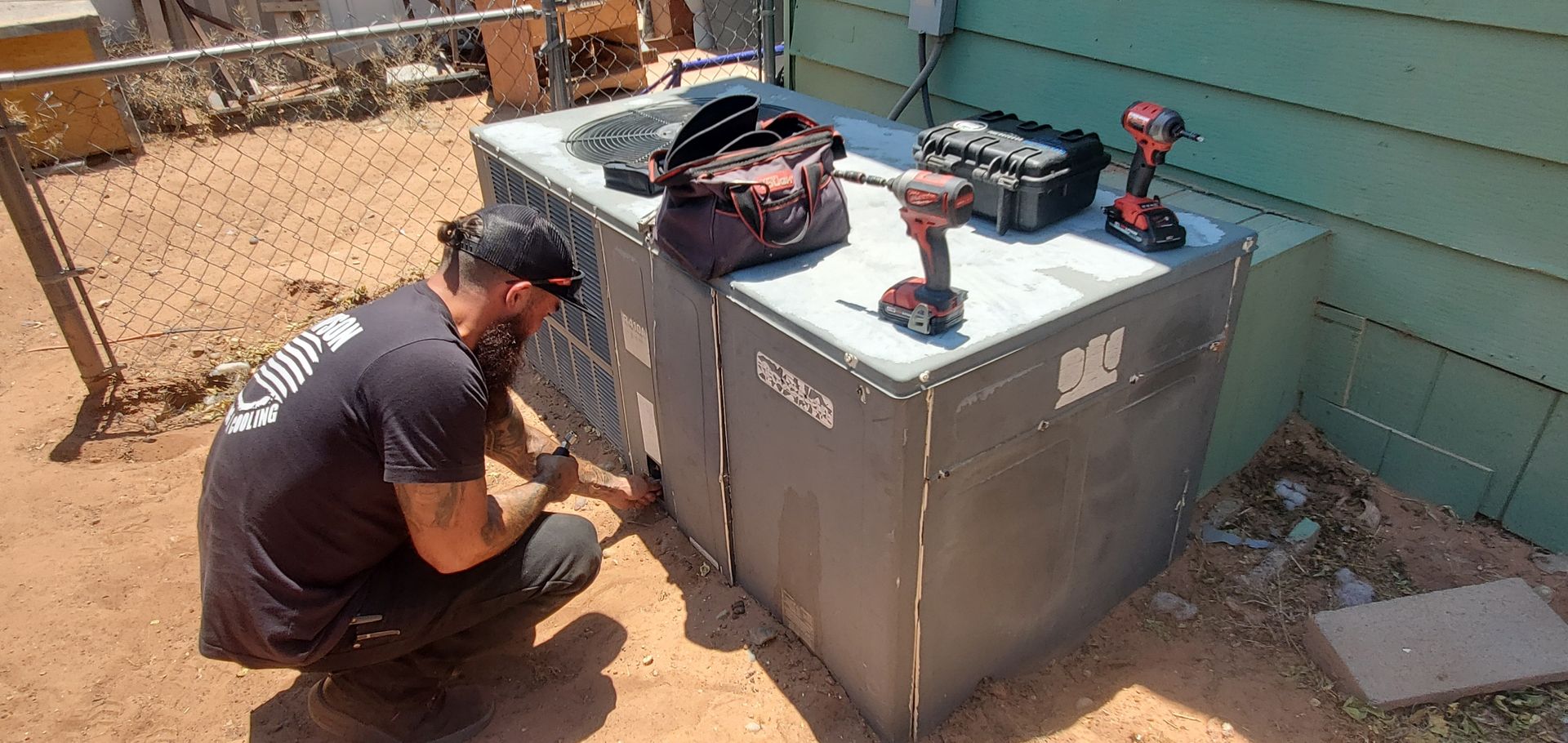 A Thompson Heating and Cooling technician is working on an air conditioner outside of a house.