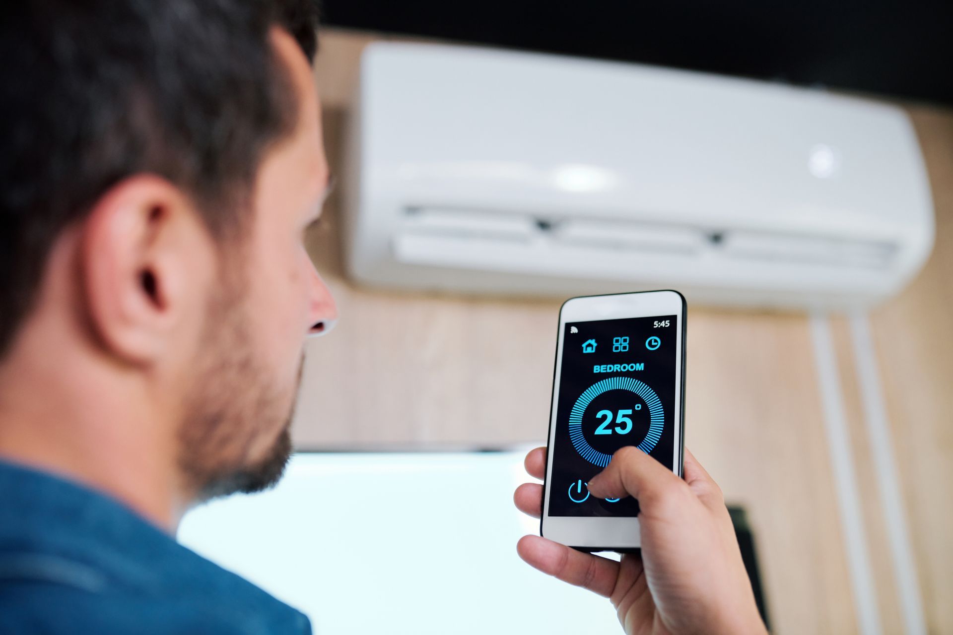 Person using a smartphone to control a wall-mounted air conditioner.