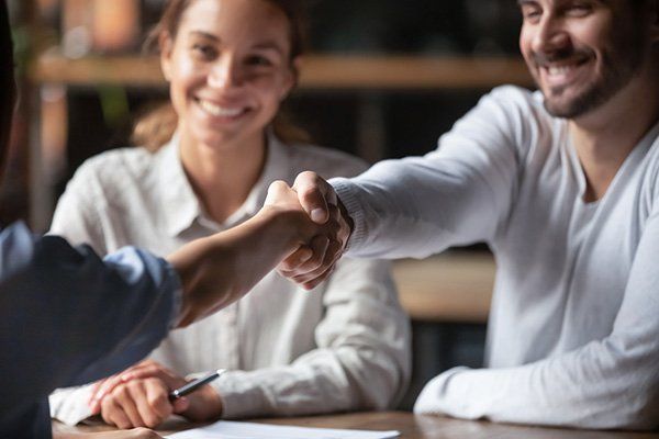 A man and woman are shaking hands while sitting at a table.