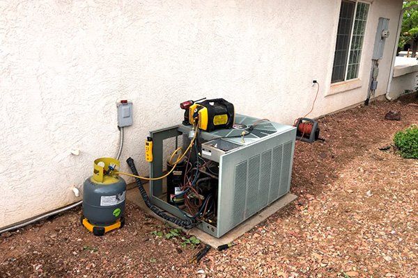 An air conditioner is being repaired in the backyard of a house.
