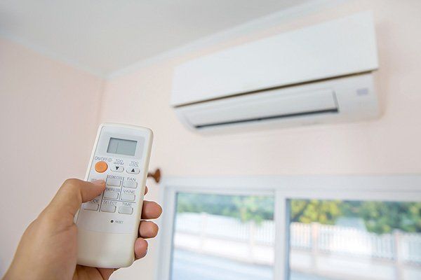 A person is holding a remote control in front of an air conditioner.