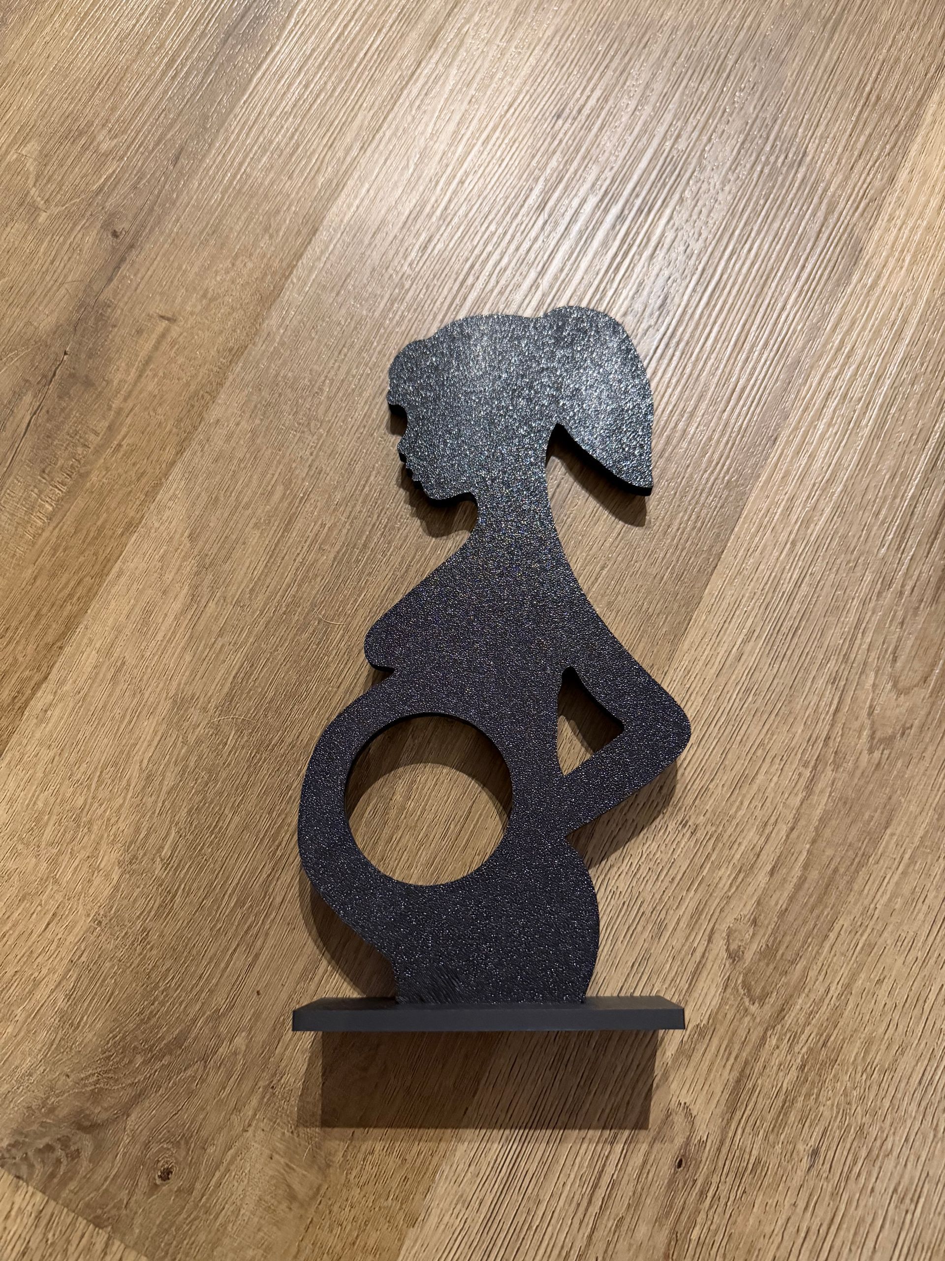 Abstracte sculptuur van zwart metaal, voorstellende een zittende mensfiguur met een cirkelvormige uitsparing