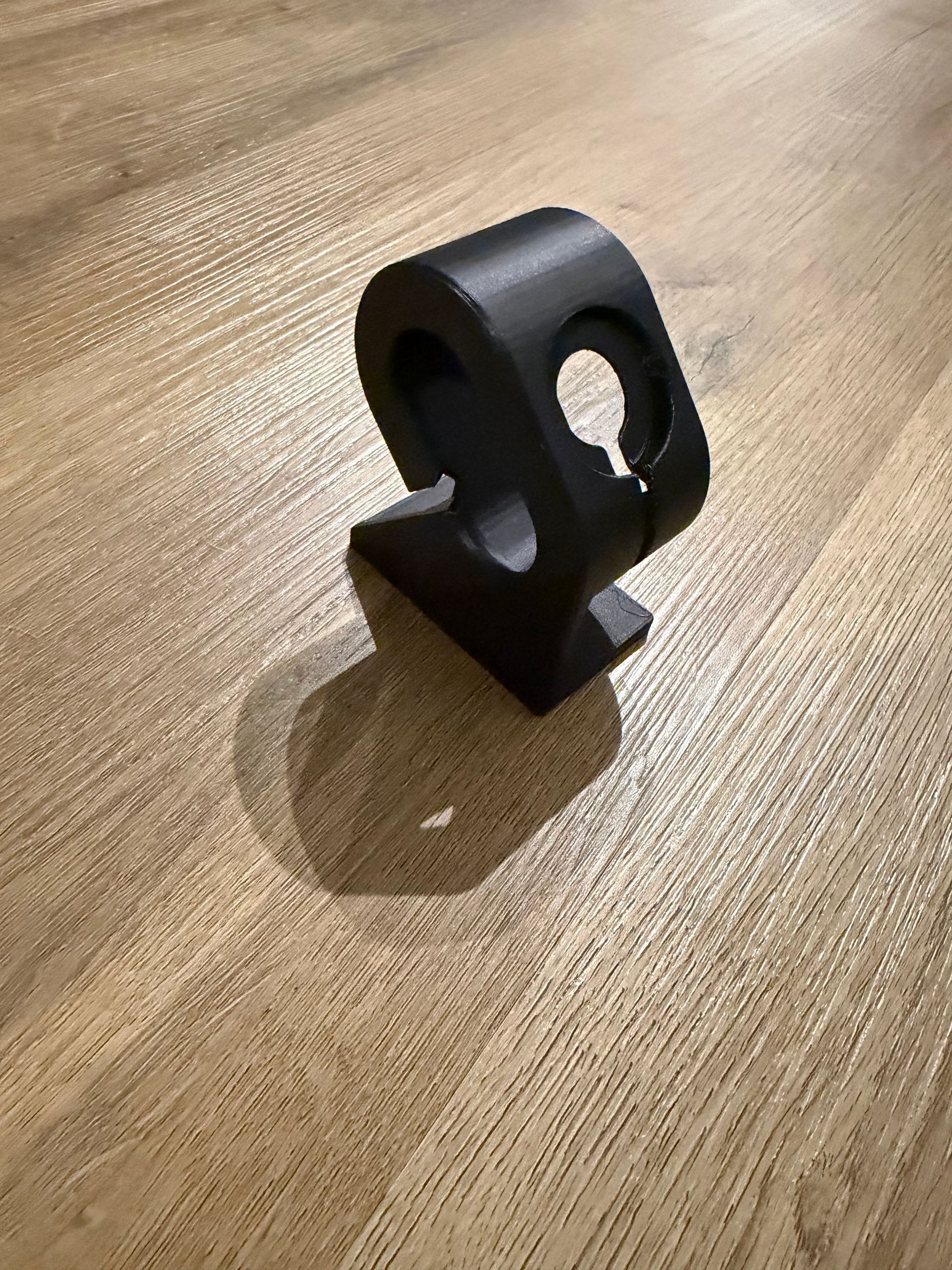 Zwarte metalen klem of beugel, staand op een houten tafelblad, met een ronde opening en een schroefgat aan de zijkant.